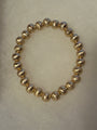 A beaded stretch bracelet made of metallic gold textured round beads, displayed on a neutral light beige background.