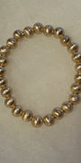 A beaded stretch bracelet made of metallic gold textured round beads, displayed on a neutral light beige background.