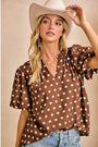 Woman wearing a brown polka dot blouse and white cowboy hat against a beige background