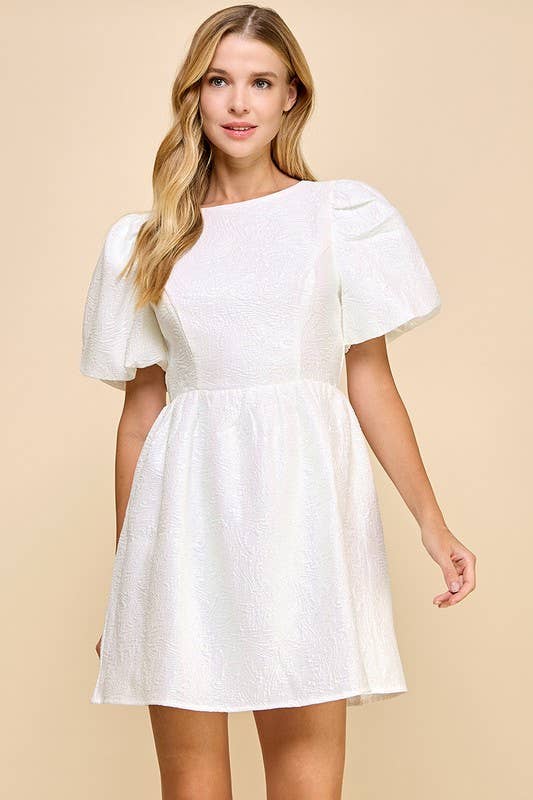 Woman wearing a white dress with puff sleeves against a beige background