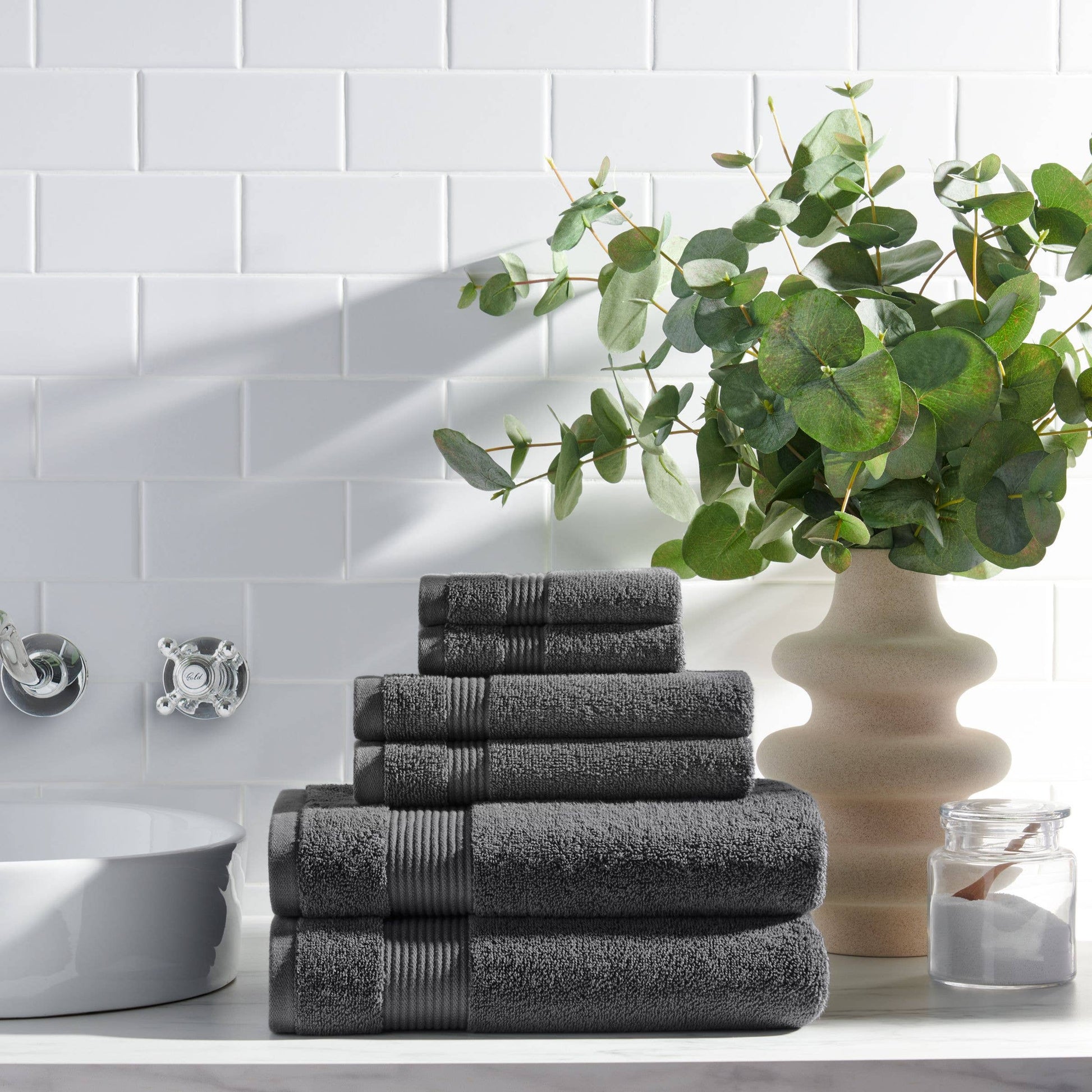 Stack of dark gray towels on a bathroom counter with a plant and decorative items.