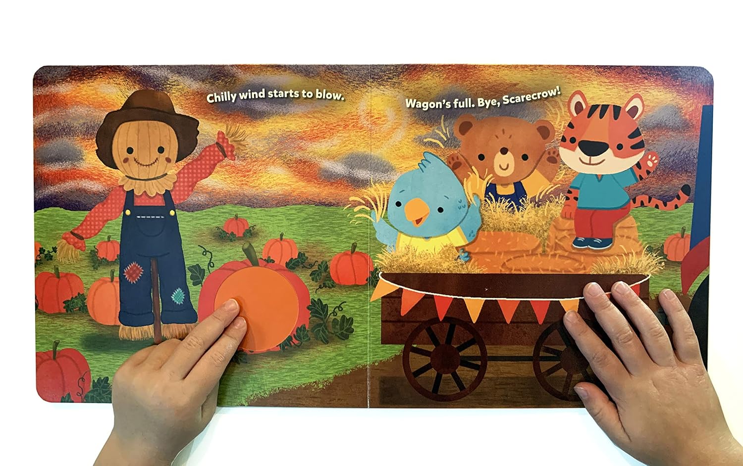 Children's book with colorful illustrations of a scarecrow, birds, and a tiger on a wagon, held open by two hands.
