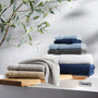 Stack of folded towels on a wooden shelf with a white tiled wall and greenery in the background