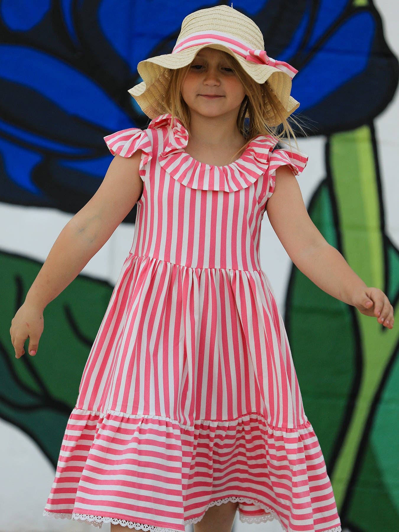 Young girl wearing a red and white striped dress with a sun hat against a colorful background