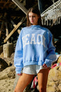 Person wearing a blue sweatshirt with 'BEACH' text on a beach setting