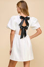 White dress with black bow detail on a beige background