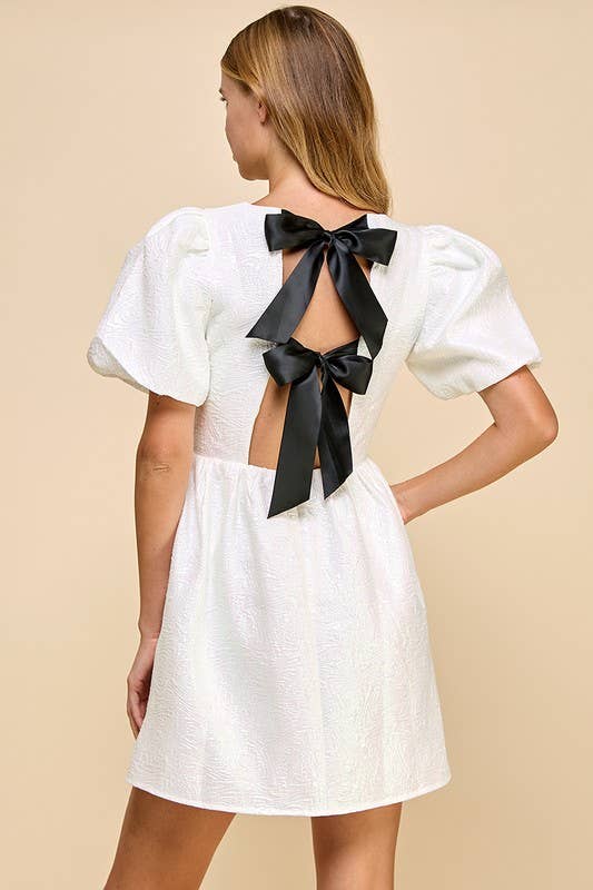 White dress with black bow detail on a beige background