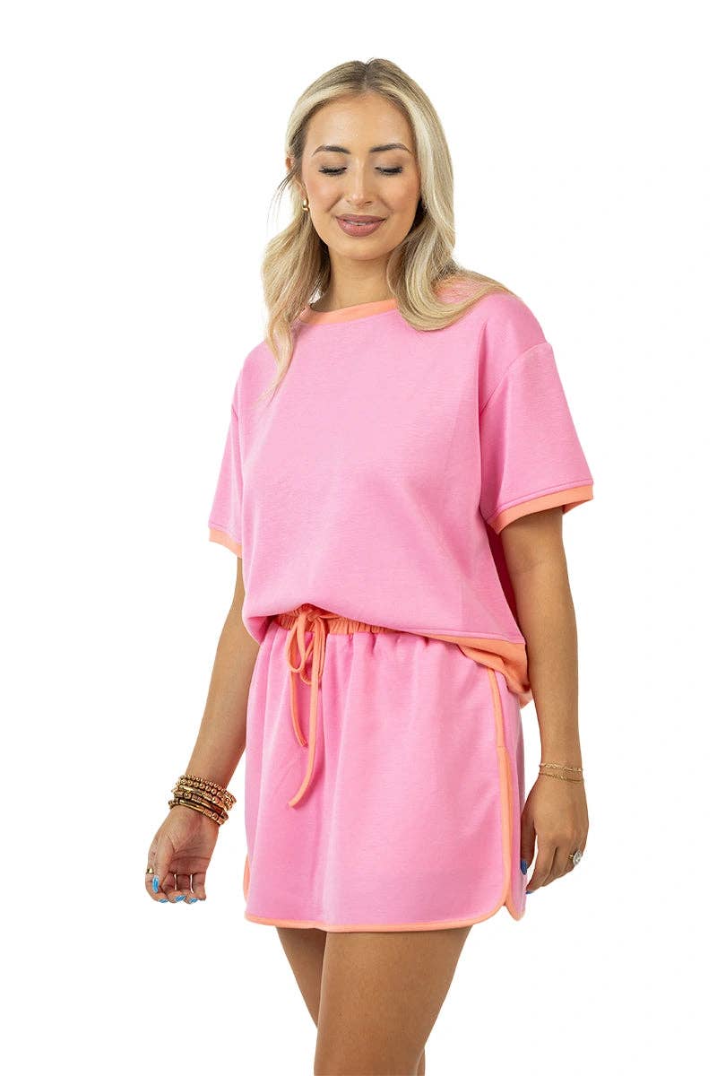 Woman wearing a pink outfit with orange trim on a white background