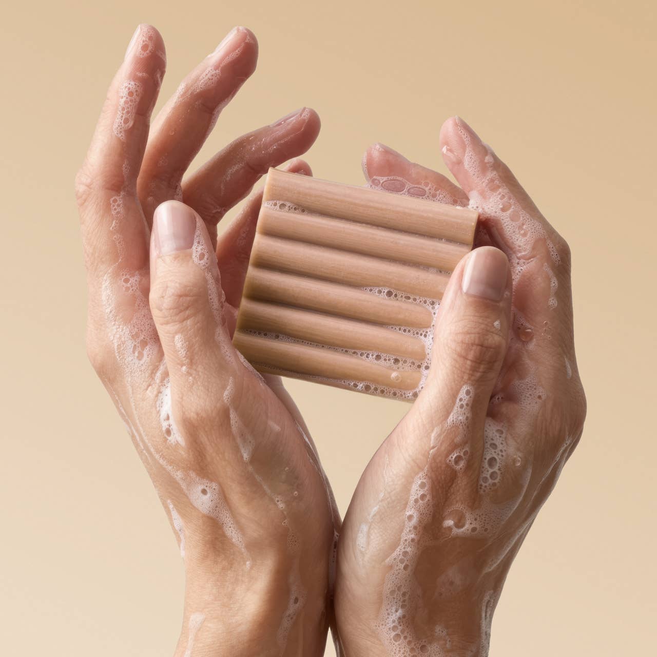 Hands holding a bar of soap with a beige background