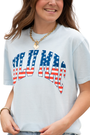 Person wearing a light blue t-shirt with 'LULU MAC' design featuring American flag colors on a white background