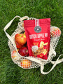Red bag of Dutch Apple Pie pretzel sticks on a mesh bag with apples on grass