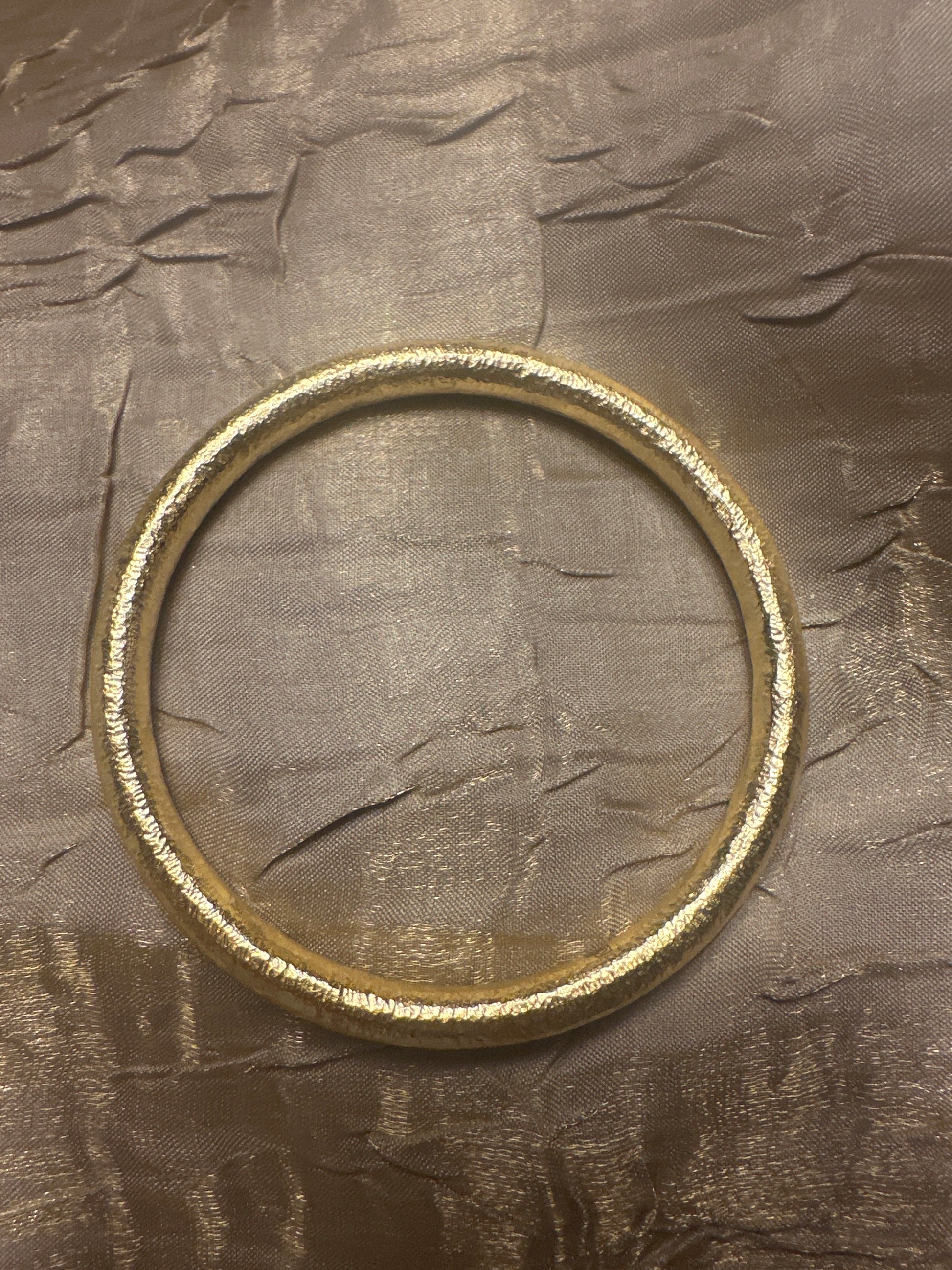 Single Gold bangle Bracelet on a gold shiny textured cloth