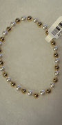 A beaded stretch bracelet featuring alternating white faux pearls and metallic gold beads, with a white barcode tag attached, shown on a textured light gray background.