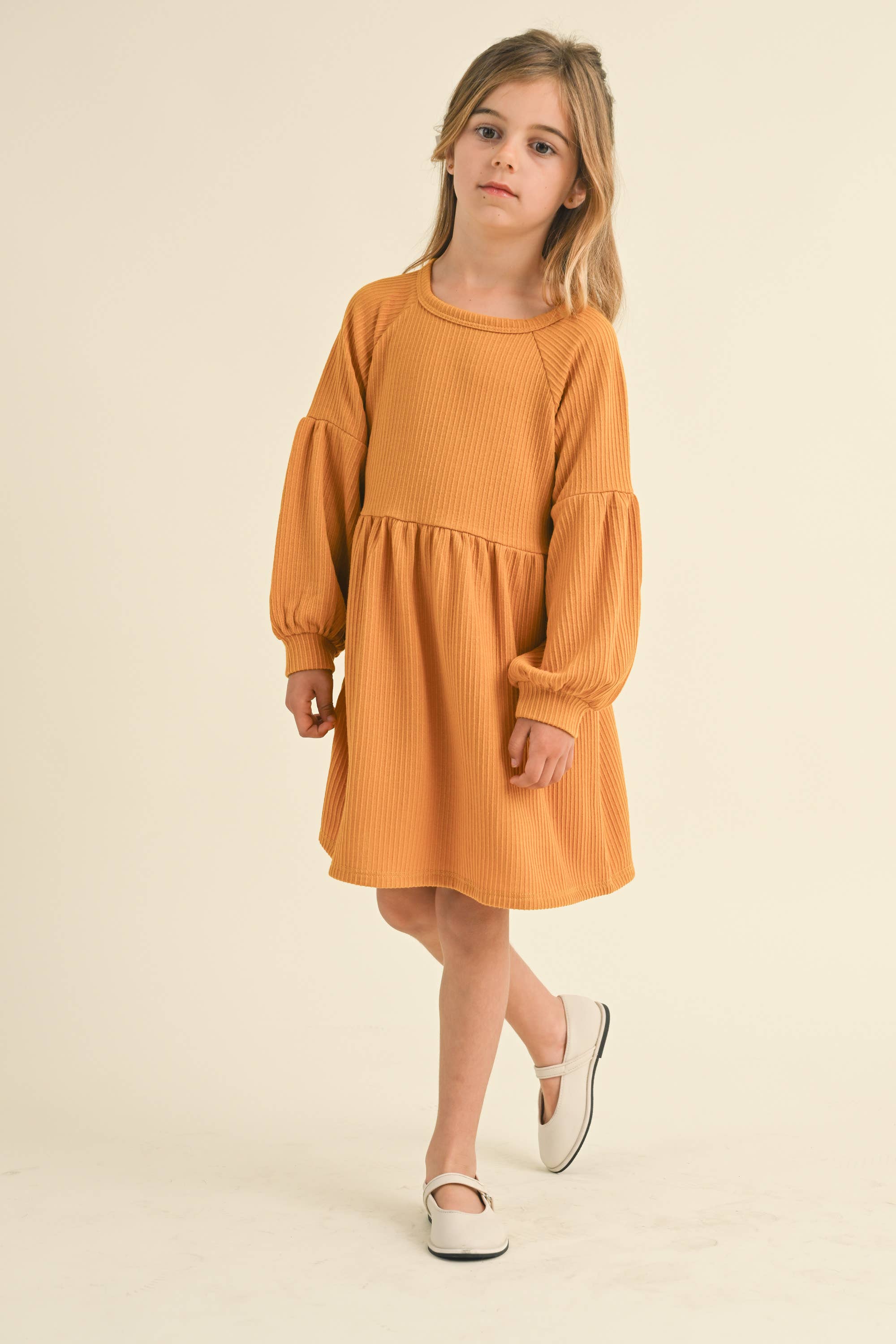 Young girl wearing an orange/mustard yellow dress on a beige background