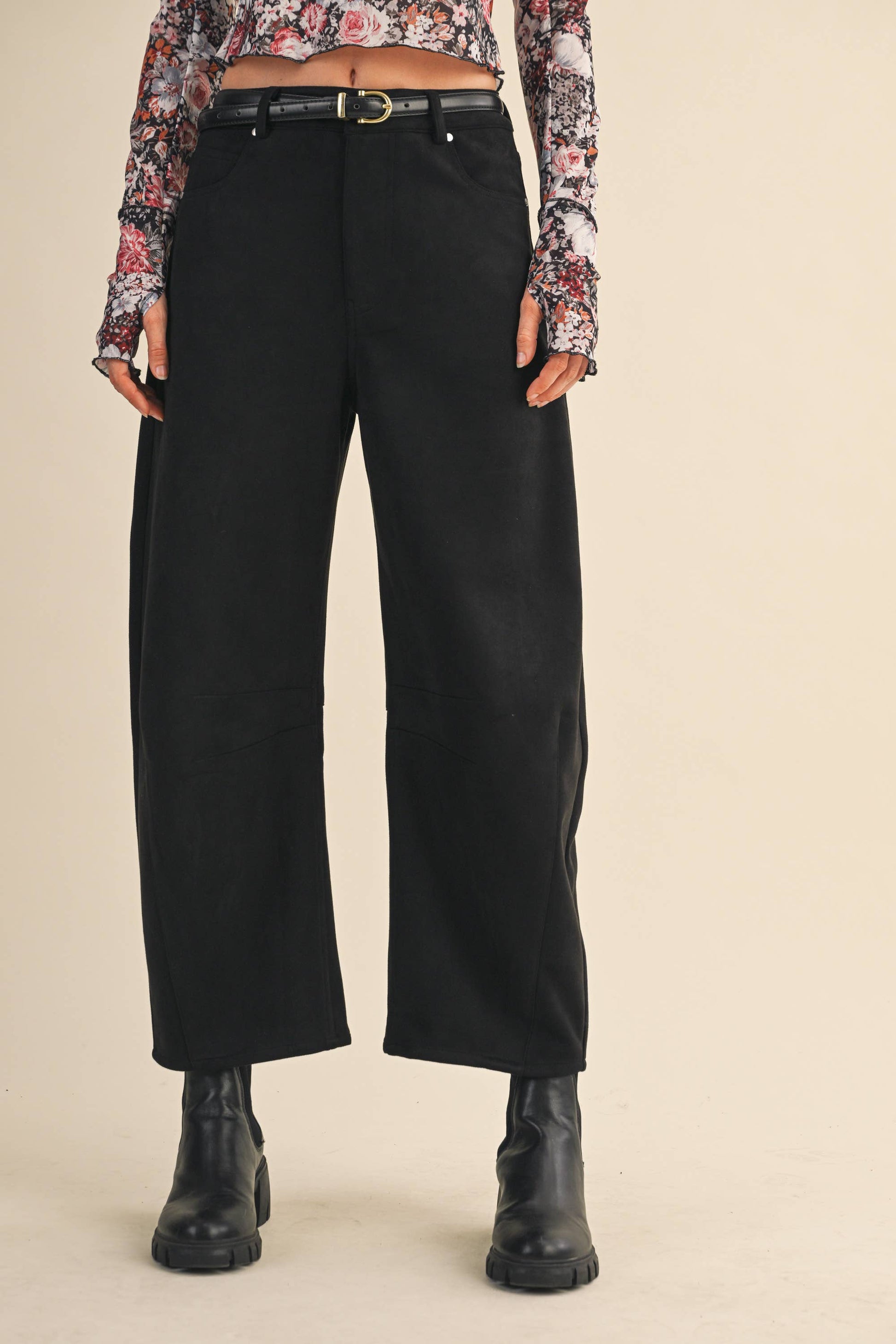 Person wearing black wide-leg pants with a floral blouse on a beige background