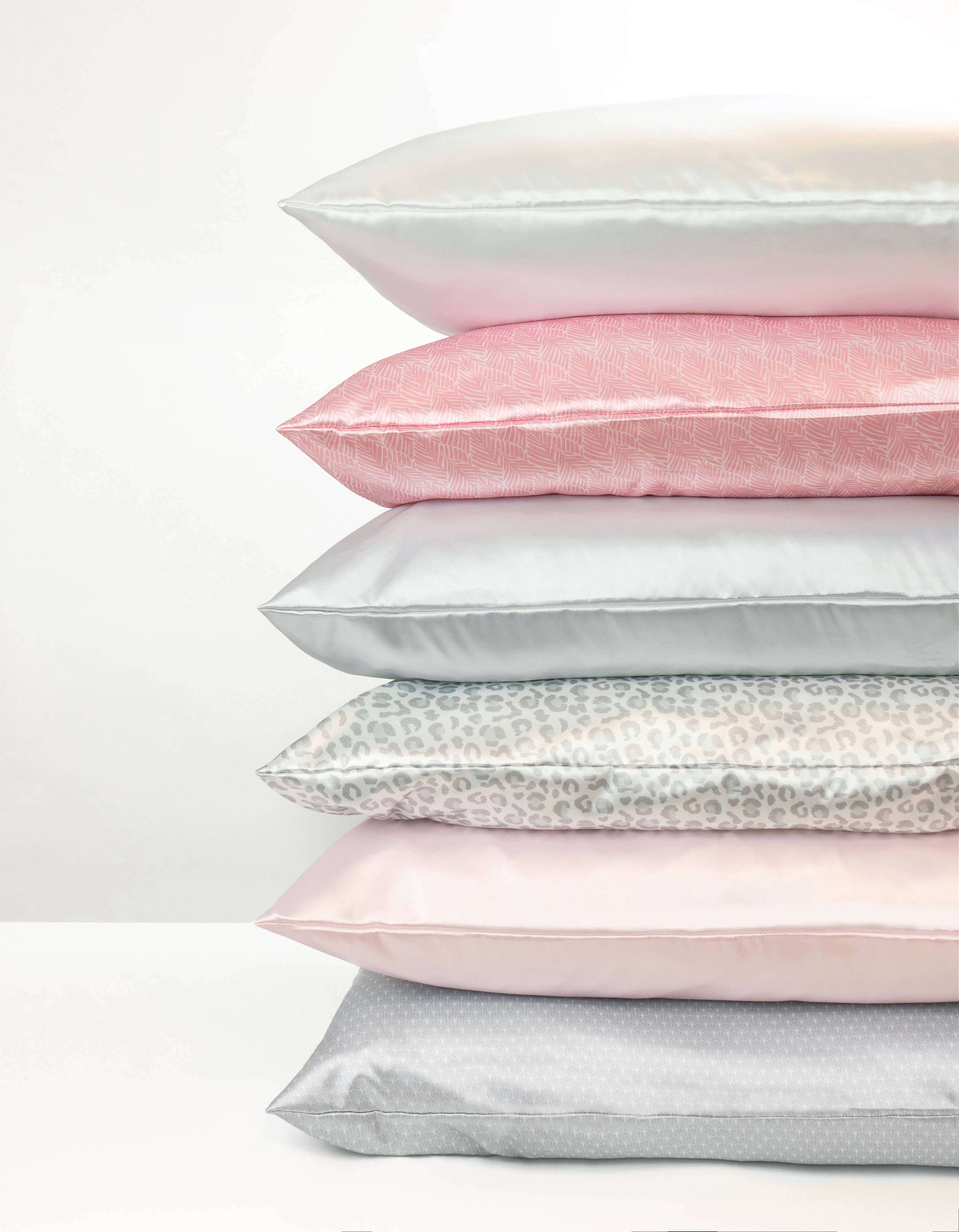 Stack of satin pillowcases in various colors on a white background