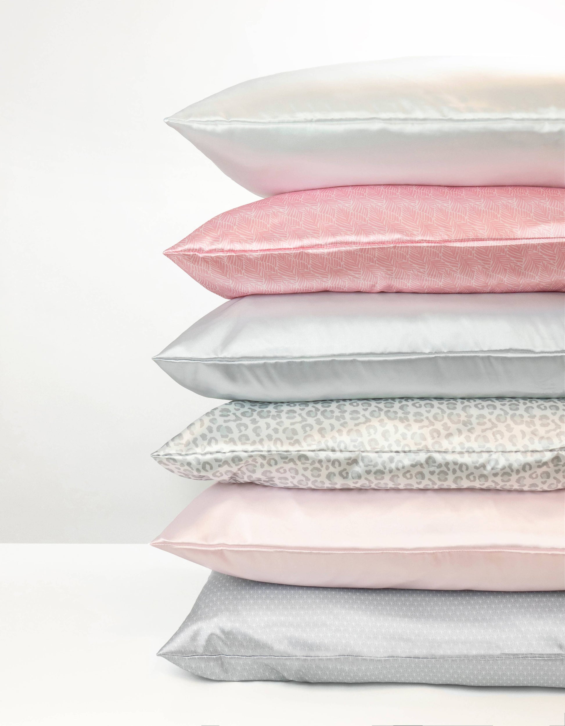 Stack of satin pillowcases in various colors on a white background
