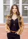 Woman wearing a tan jacket over a black top with long, wavy hair.