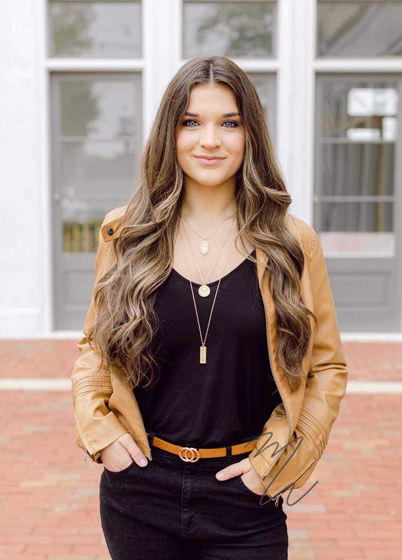 Woman wearing a tan jacket over a black top with long, wavy hair.