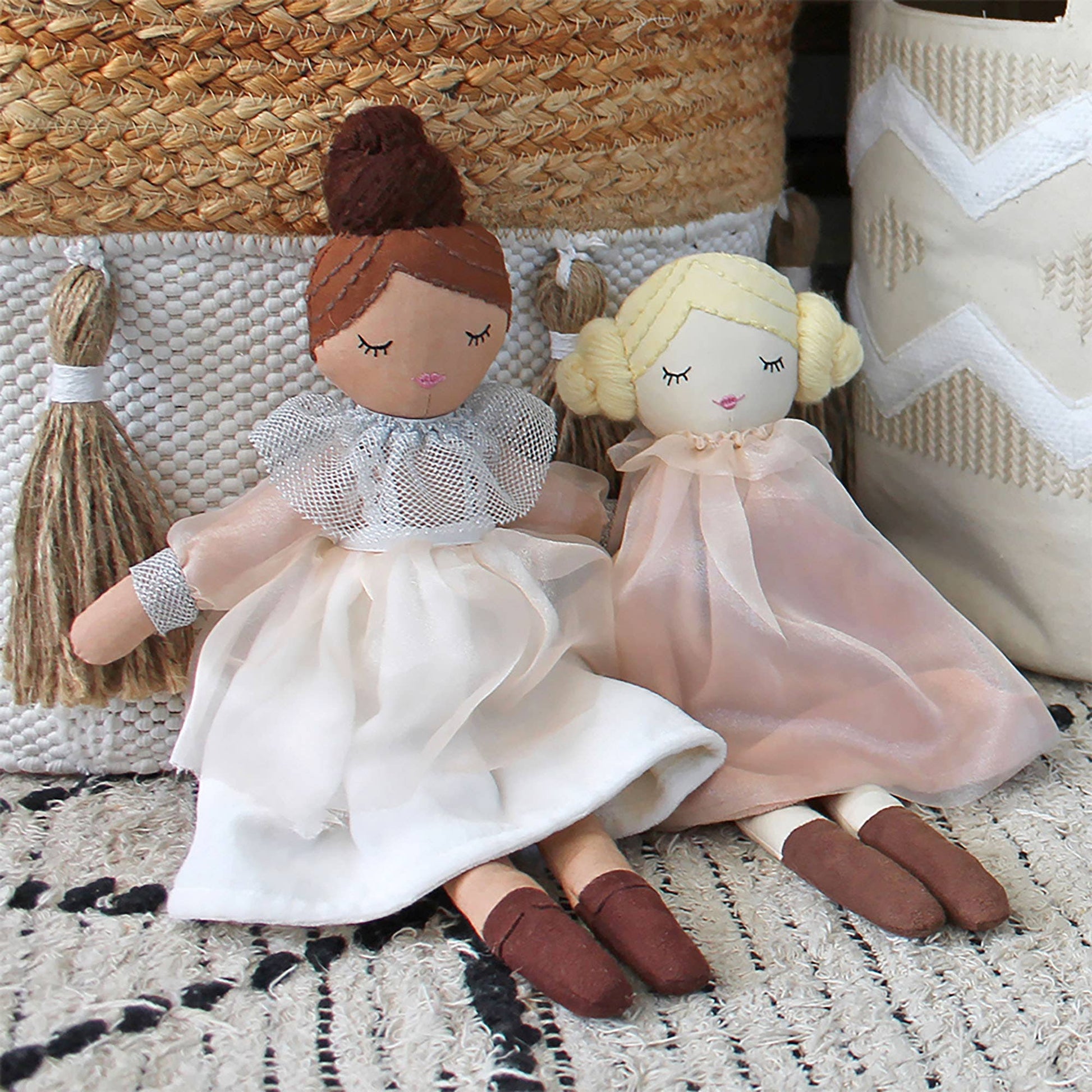 Two dolls with white and pink dresses sitting on a textured surface.