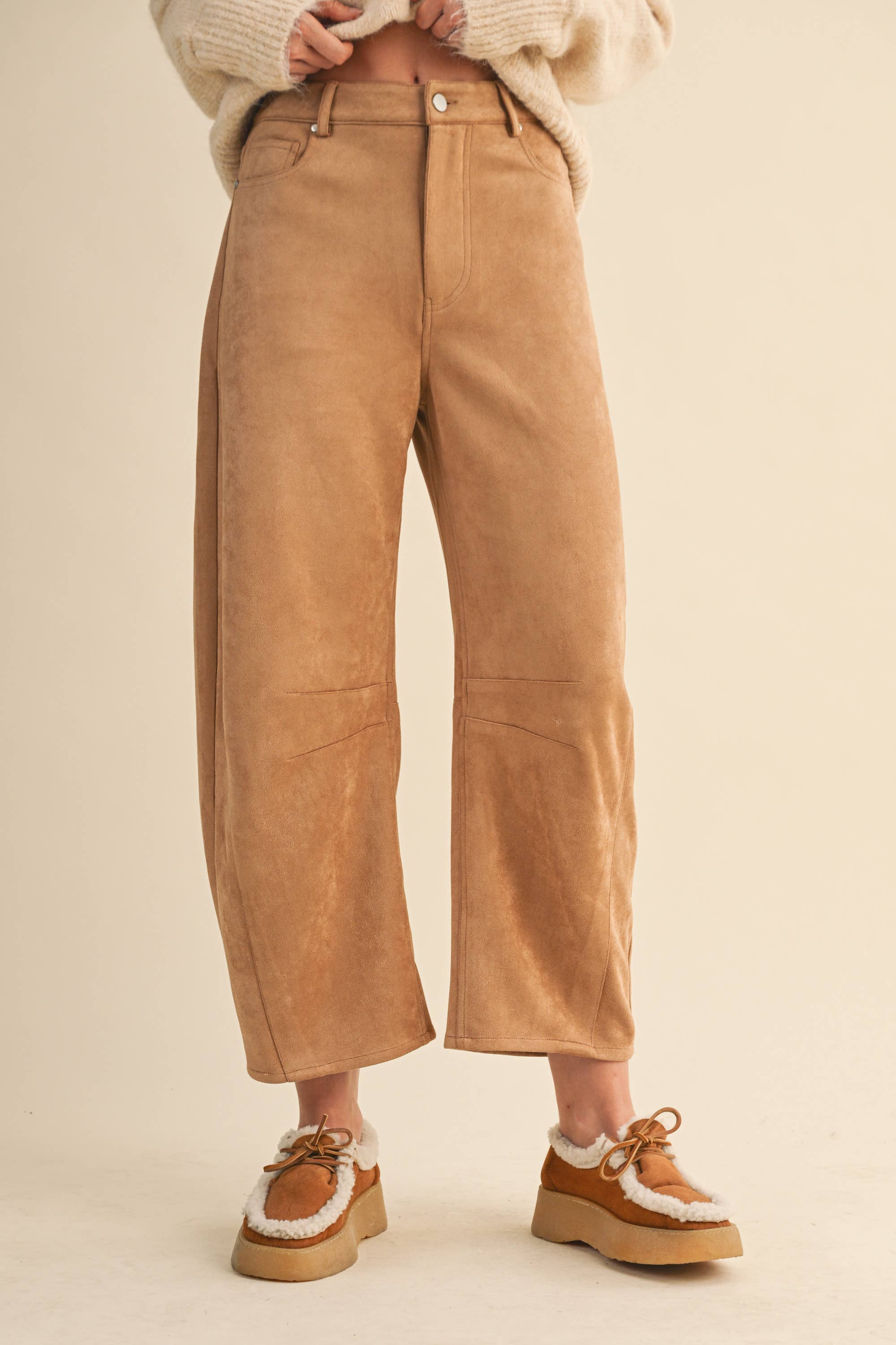 Tan suede pants worn by a person on a beige background