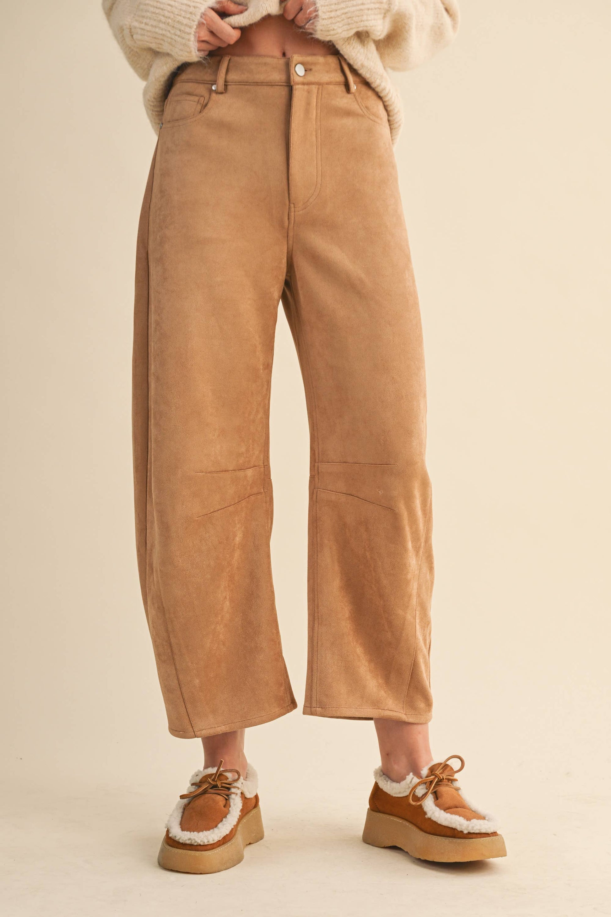 Tan suede pants worn by a person on a beige background