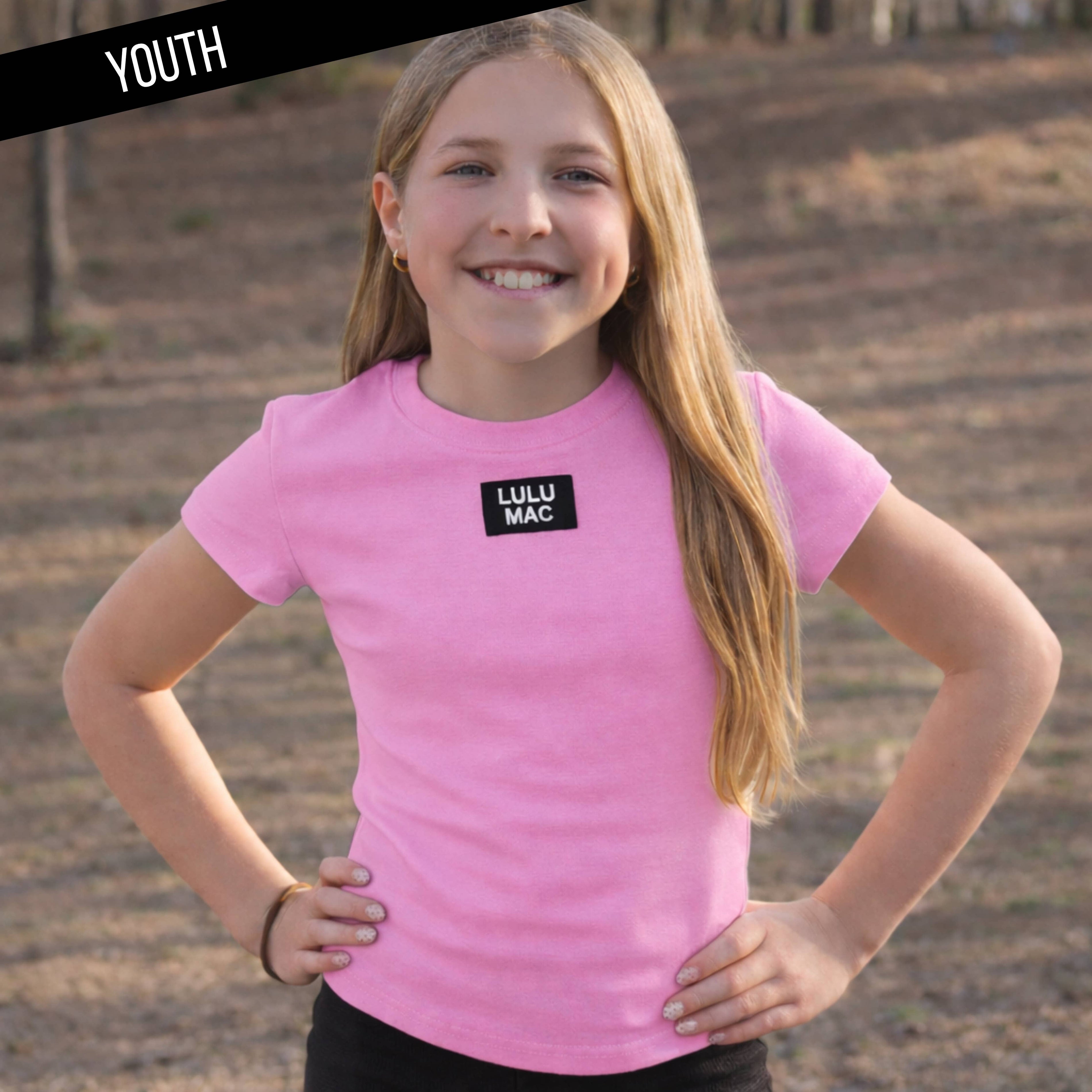 Young girl wearing a pink 'Lulu Mac' t-shirt outdoors.