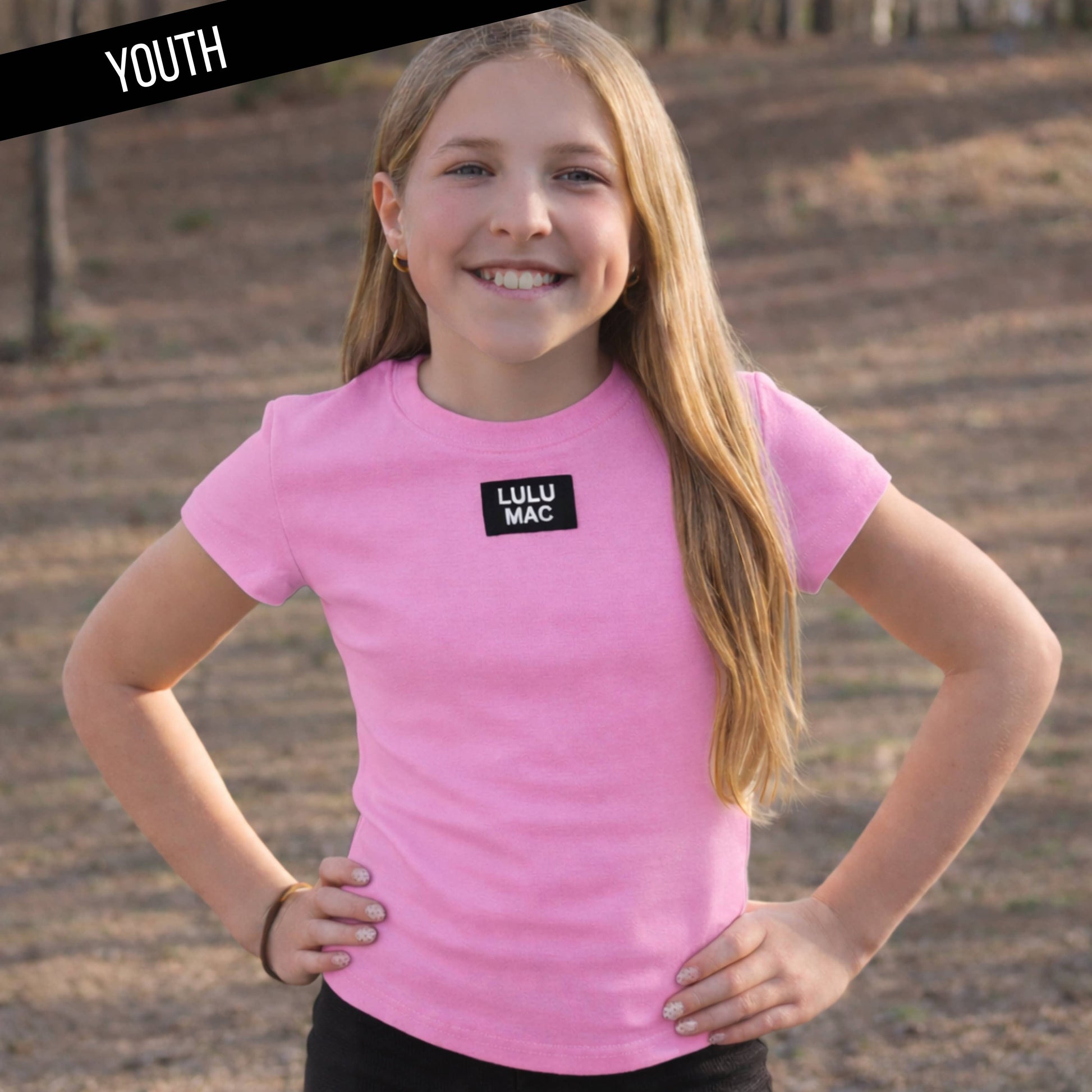 Young girl wearing a pink 'Lulu Mac' t-shirt outdoors.