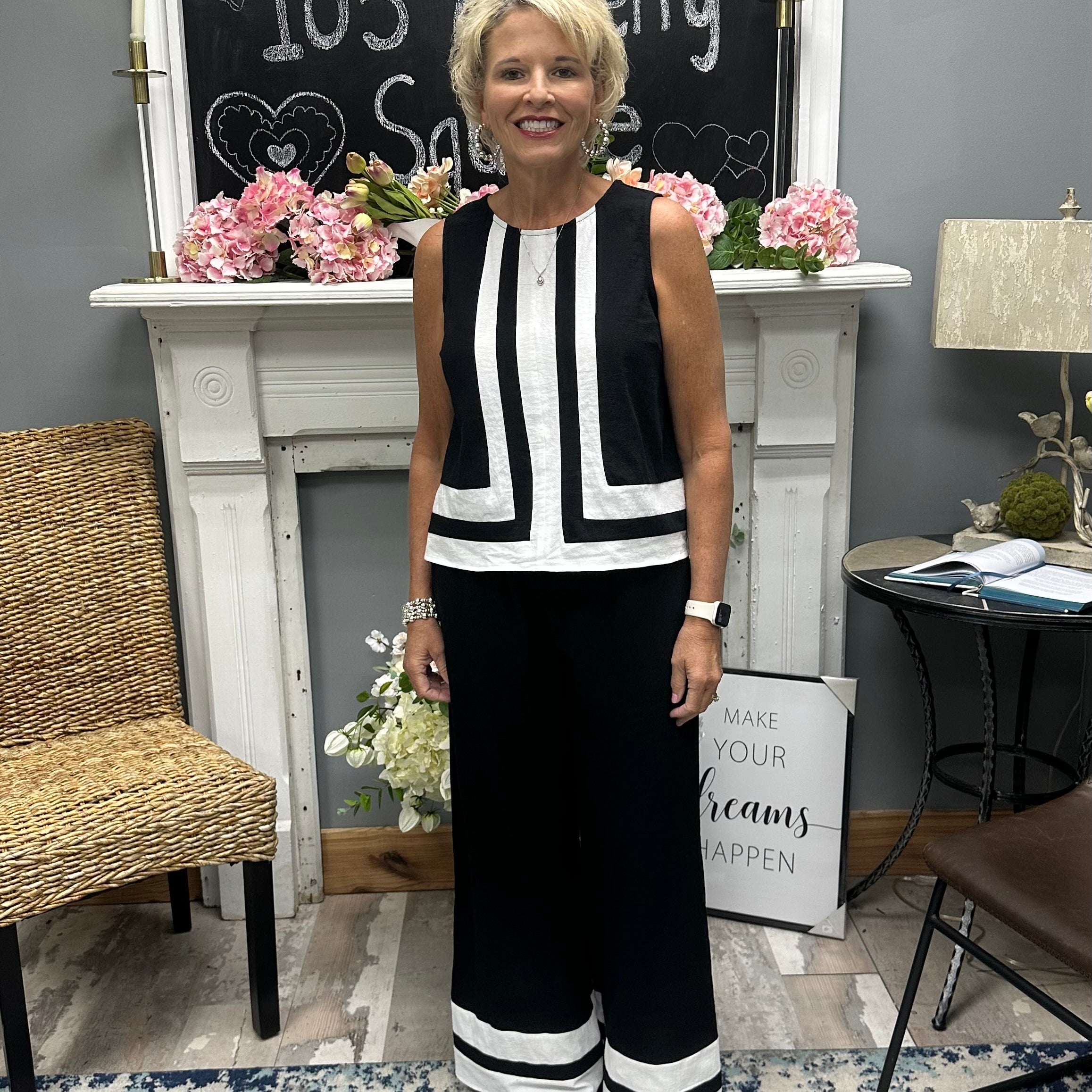 Woman in a black and white outfit standing in a room with a fireplace and decorative items.