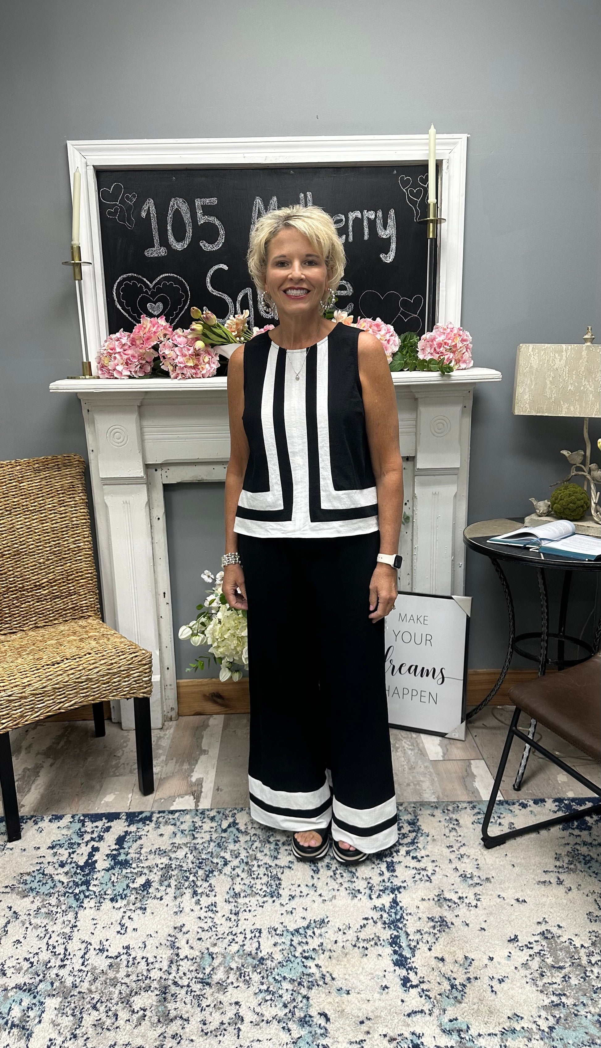 Woman in a black and white outfit standing in a room with a fireplace and decorative items.