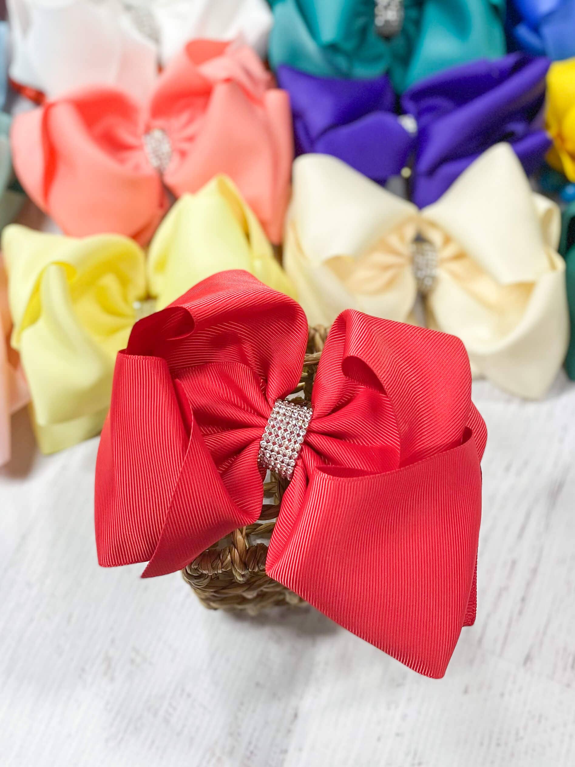 Red hair bow with a rhinestone center on a white surface with other colorful bows in the background.