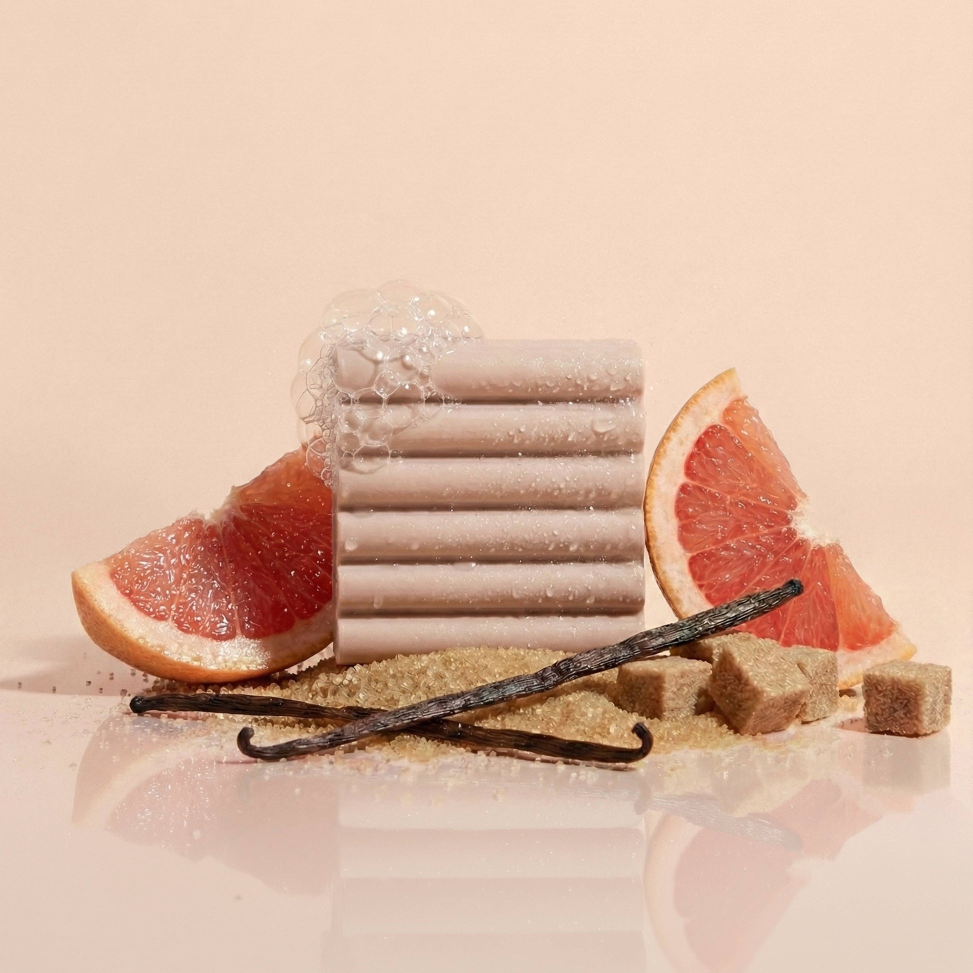 Stack of soap bars with grapefruit slices and vanilla beans on a beige background