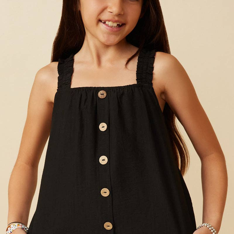Young girl wearing a black sleeveless top with buttons on a beige background
