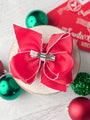 Red hair bow with a silver clip on a white surface with Christmas ornaments.