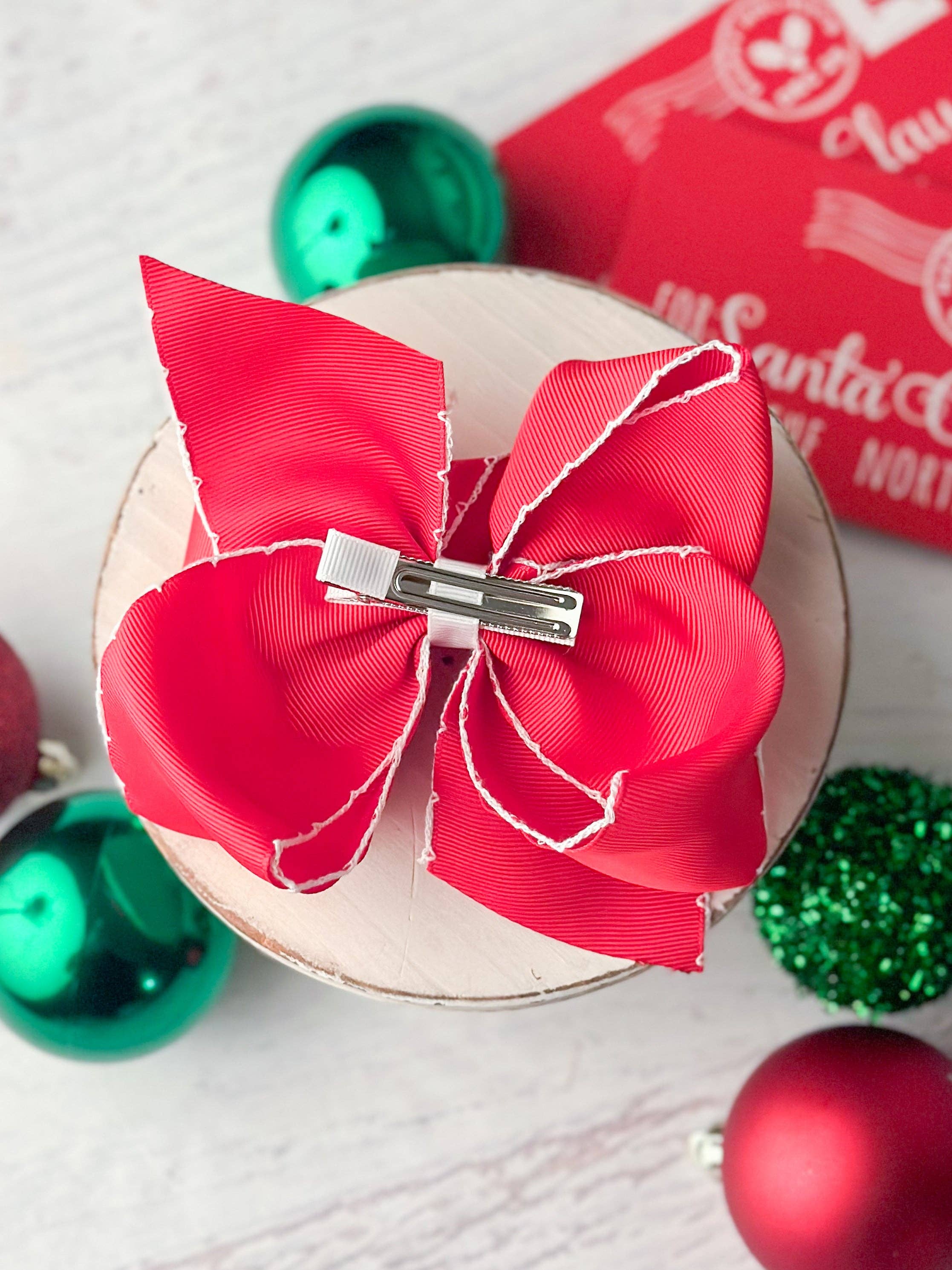 Red hair bow with a silver clip on a white surface with Christmas ornaments.