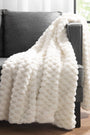 White textured blanket draped over a gray sofa in a room with large windows.