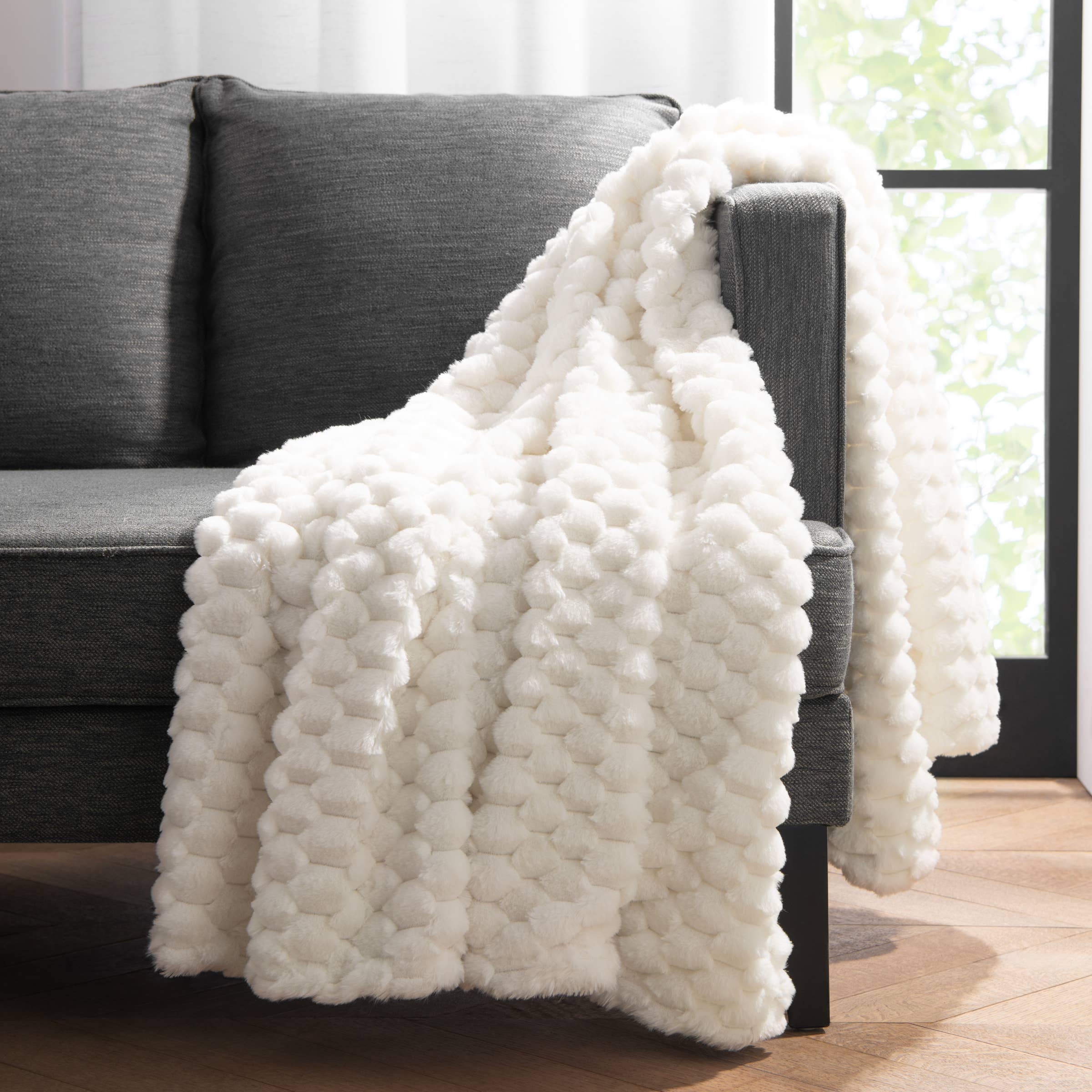 White textured blanket draped over a gray sofa in a room with large windows.