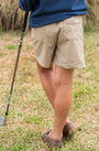 Person wearing beige shorts and a blue top, standing on grass with a golf club.