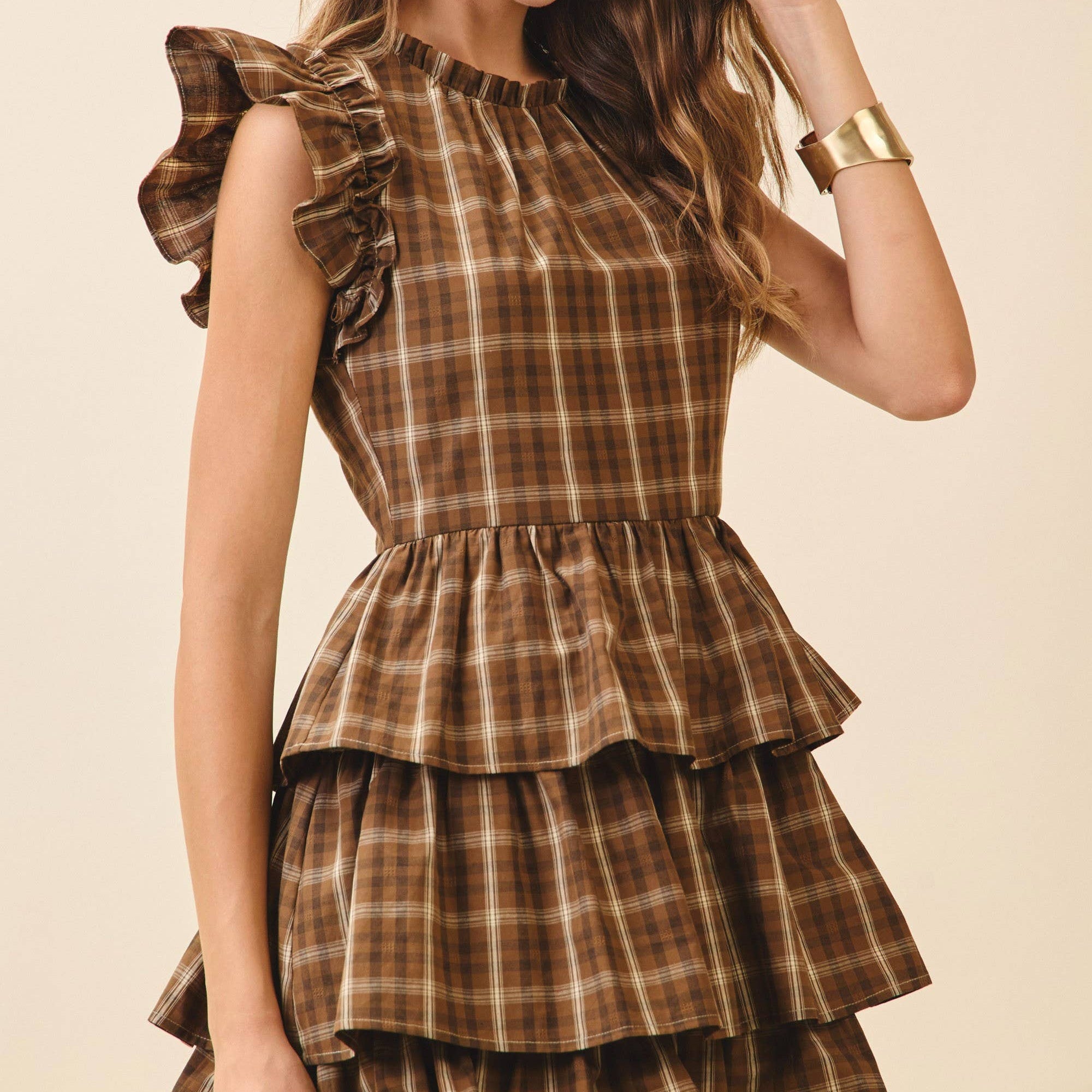 Woman wearing a brown plaid dress with ruffled layers on a beige background
