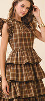 Woman wearing a brown plaid dress with ruffled layers on a beige background