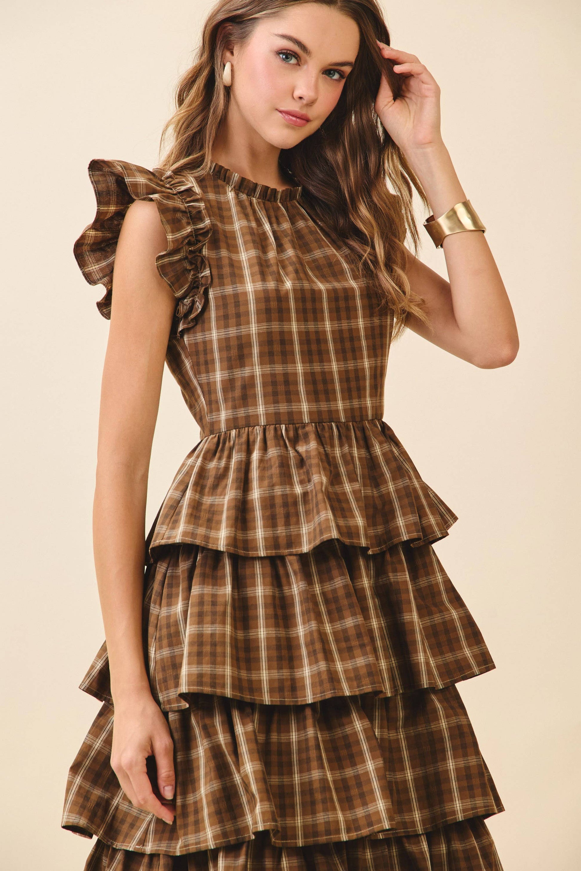 Woman wearing a brown plaid dress with ruffled layers on a beige background