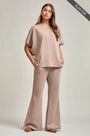 Woman wearing a beige outfit with wide-leg pants on a plain background