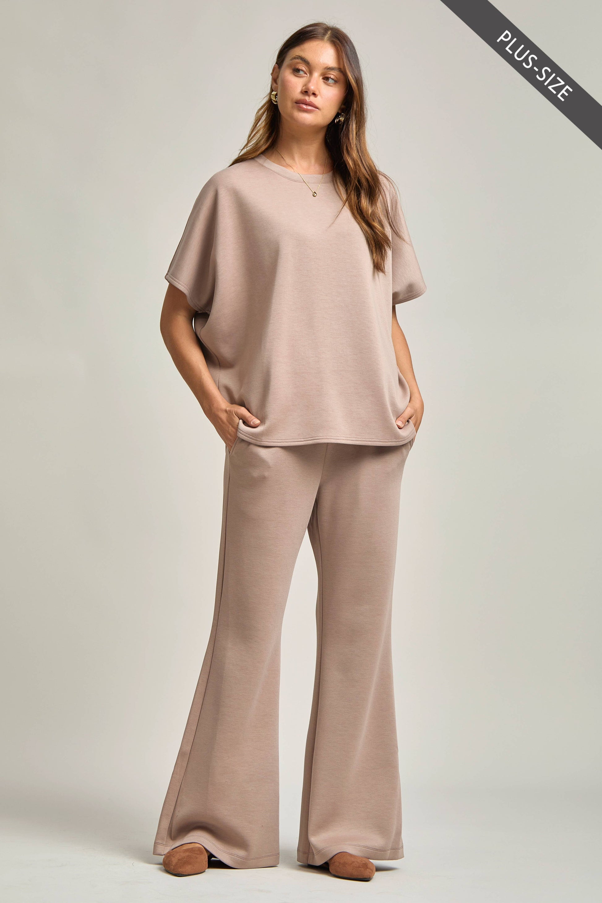 Woman wearing a beige outfit with wide-leg pants on a plain background