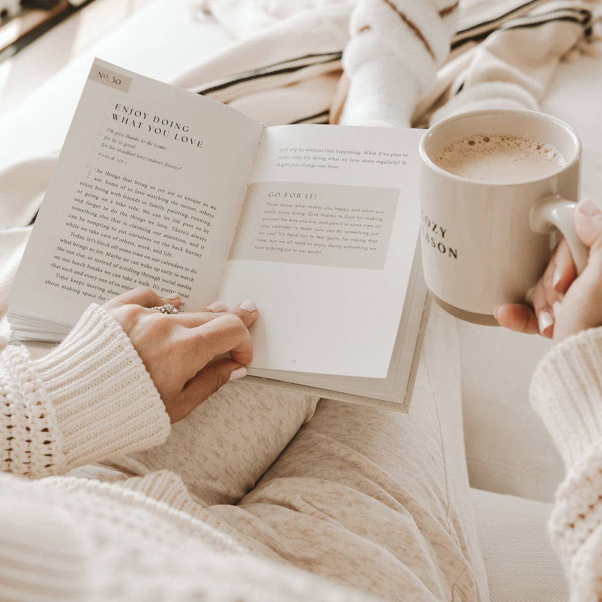 Open devotional book on a couch with coffee cup beside pages and reading hands