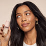 Woman holding kitsch warm sugar hair and body product with a neutral background