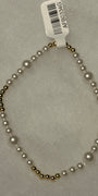 A beaded necklace with white faux pearls and small metallic gold beads, shown on a light gray textured background with a white barcode tag attached.