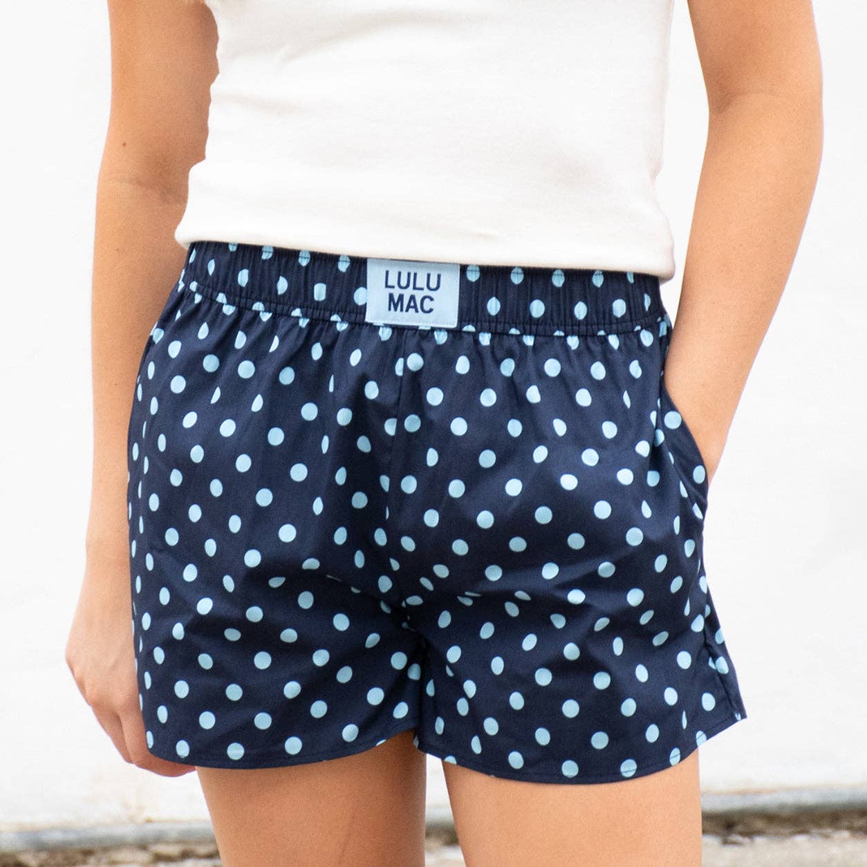 Navy blue shorts with white polka dots worn by a person on a light background