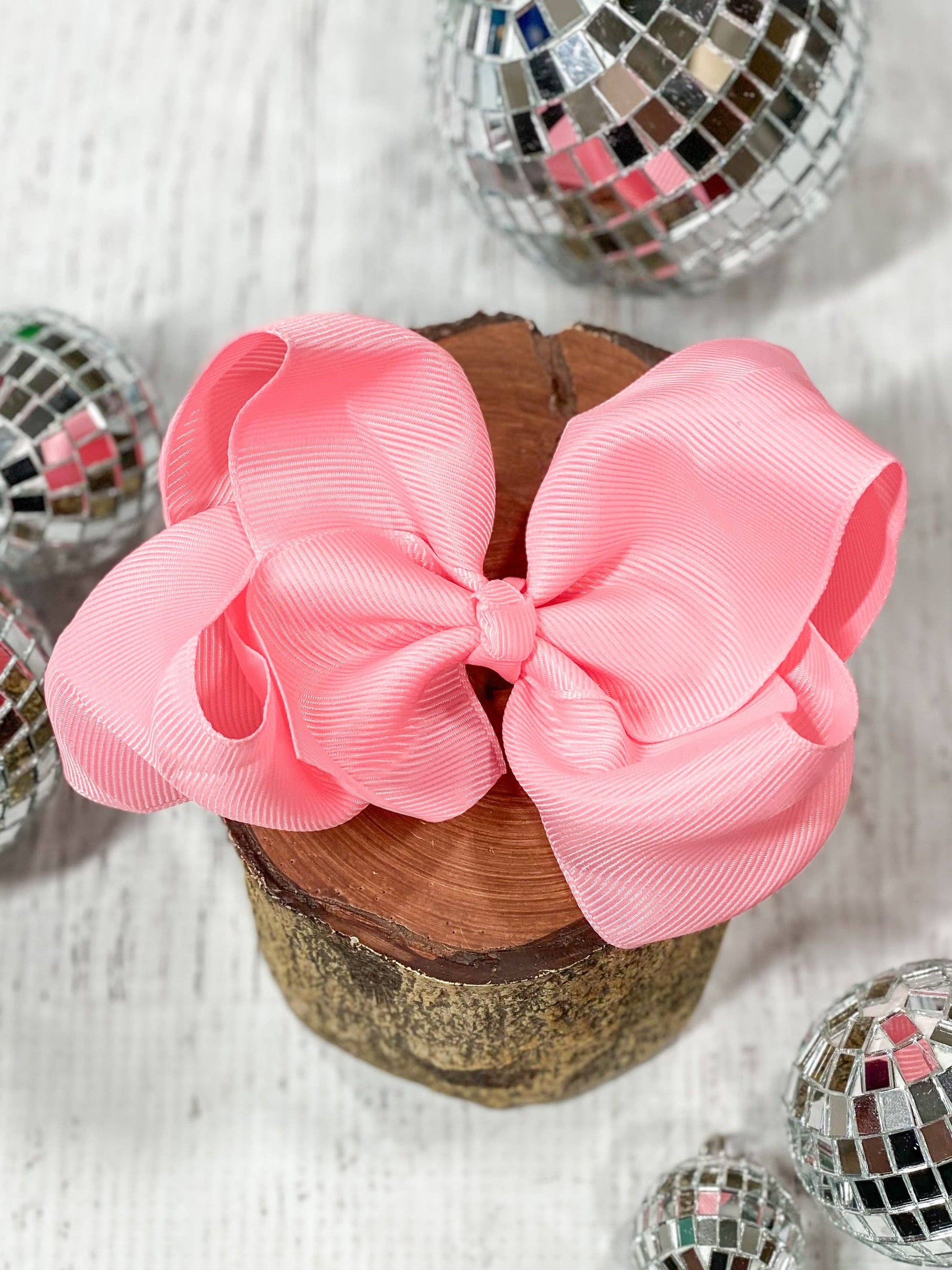 Large pink bow on a wooden block with disco balls in the background