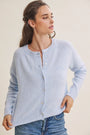 A woman wearing a light blue knit cardigan sweater with a button-up front, paired with blue jeans, against a plain beige background.