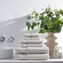 Stack of gray towels on a bathroom counter with a vase of greenery and white tiles in the background.
